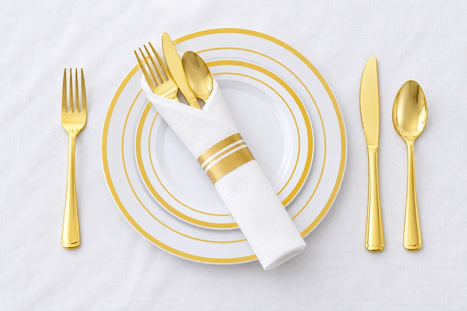 White gold-rim plates with gold cutlery and a rolled white napkin on a white tablecloth