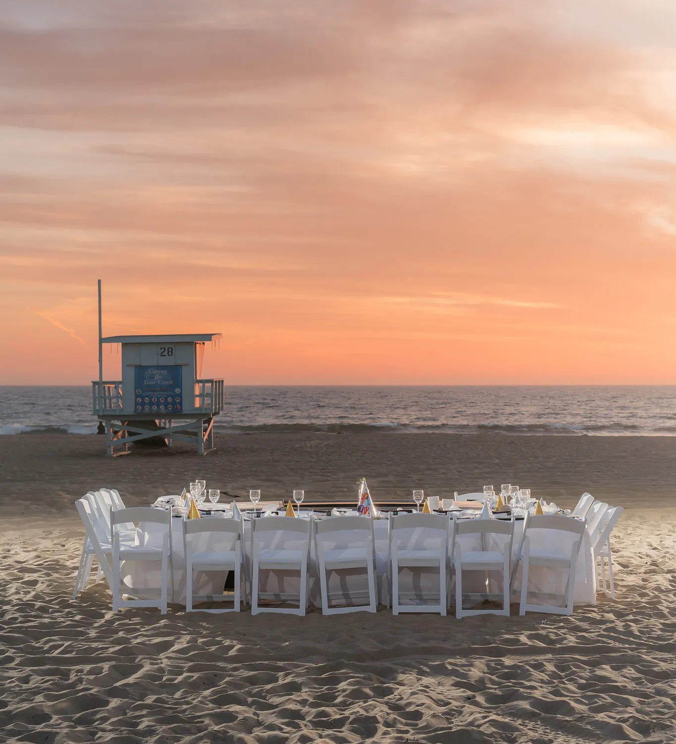 Long dinner table set on the sand at sunset for a hibachi party in San Pedro