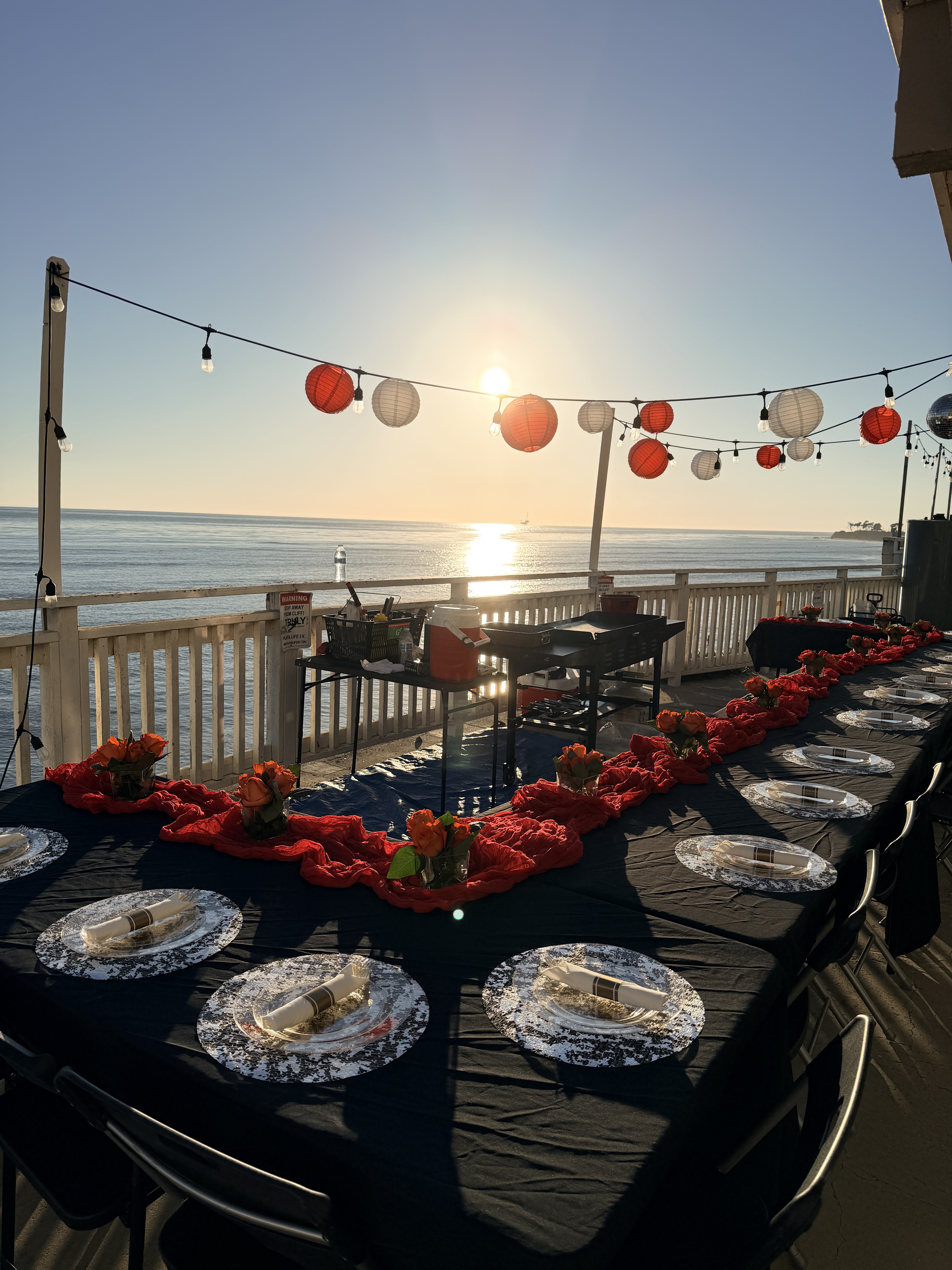 Oceanfront sunset party table with lanterns and roses